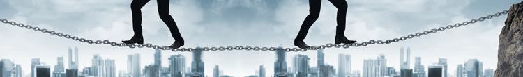 B2B Challenges Two pairs of legs walk a tightrope made of metal chain links, with a city skyline in the background.