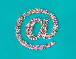 The 'at' symbol made from hundreds-and-thousands sprinkles on a turquoise background.