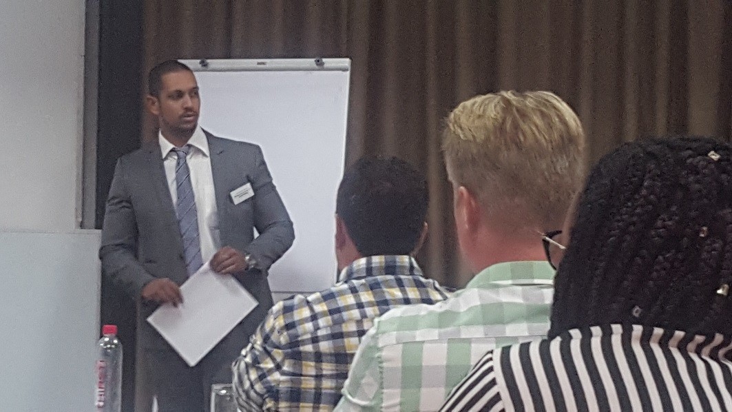 Mohamed Moosa A man in a suit and tie addresses three people, seated in rows.