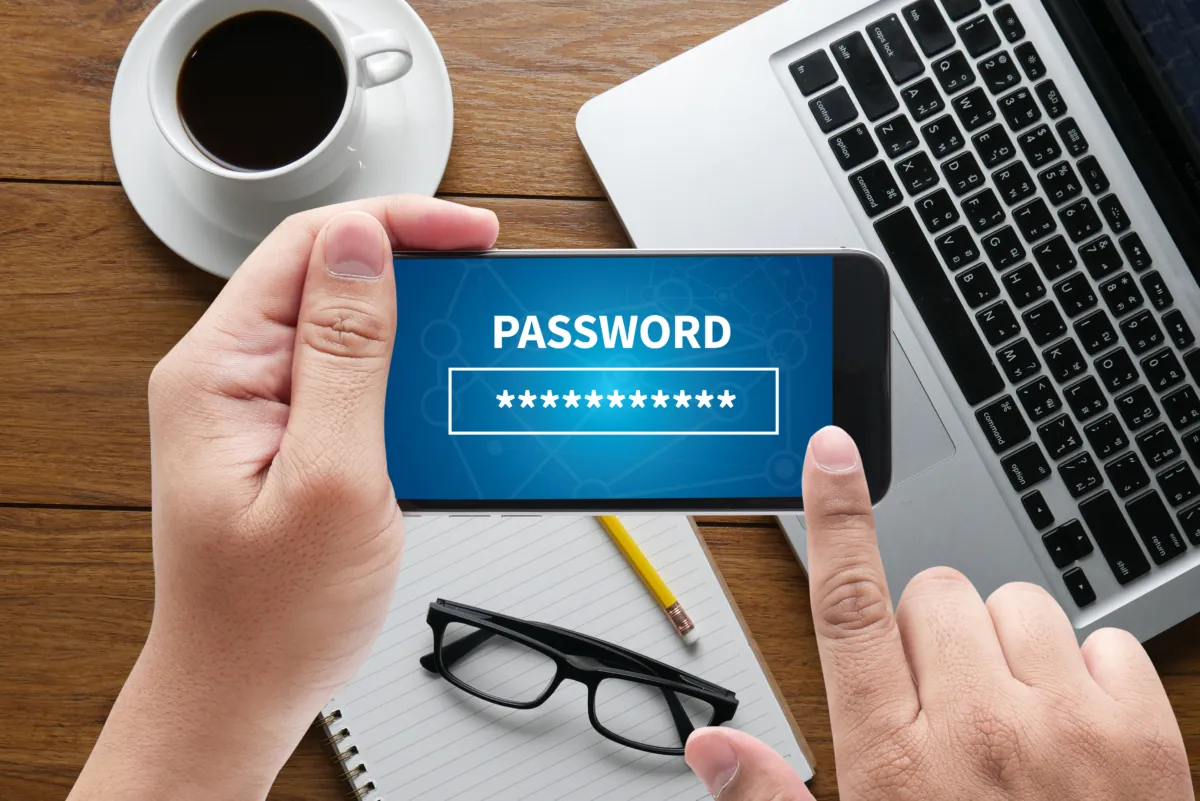 The importance of single sign-on in email signature software 10 Hands holding a mobile device horizontally over a desk with a laptop, notepad and cup of coffee. Mobile device has a hidden password on the screen