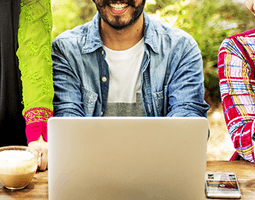 A close-up of a man sitting behind a laptop, with people either side.
