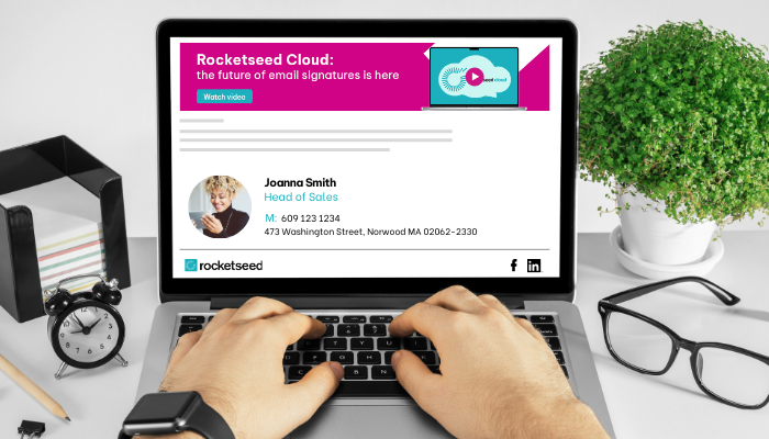 Seven Ways Rocketseed Cloud's Azure Servers Save IT Teams Email Signature Management Time 1 Top view of hands on a laptop. The laptop screen has a branded business email signature from Rocketseed with an email marketing banner promoting Rocketseed Cloud - the future of email signatures