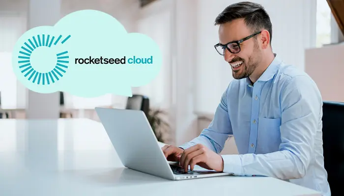 Rocketseed Expands Global MSP Partner Program with Advanced Cloud Email Signature Management 16 A smiling man, sitting behind a desk working on his laptop with a Cloud Image and the wording: Rocketseed Cloud